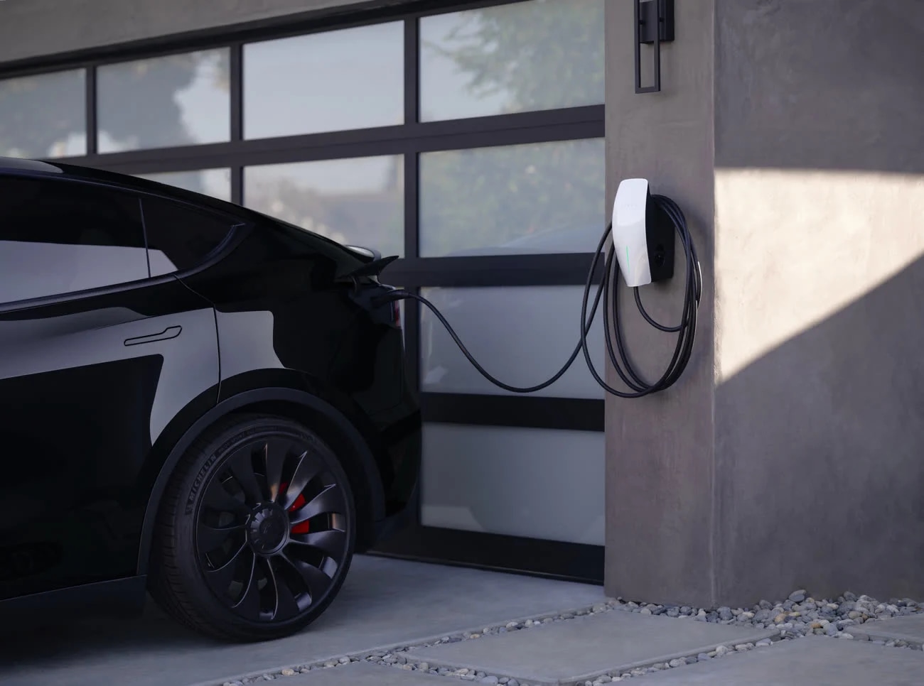 Véhicule Tesla noir en charge devant un garage moderne
